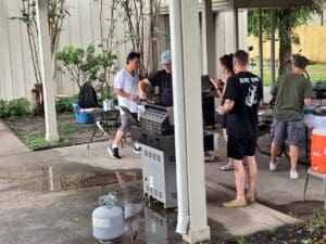 A group of people standing around an outdoor grill.